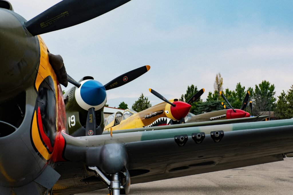 Close-up view of vintage fighter planes with colorful propellers displayed outdoors on a clear day.
